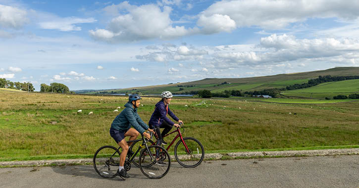 couple cycling through the Durham Dales countryside on a bright sunny day, Balderhead Reservoir, County Durham